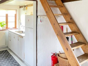 Une cuisine avec des meubles blancs, une échelle en bois, un extincteur et une fenêtre avec des rideaux.