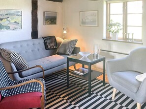 A living room with a grey sofa, patterned armchairs, a glass coffee table, and a window with plants. - 6 Person Holiday Home in Degeberga (Degeberga)