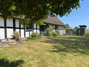 A traditional half-timbered house with a thatched roof, a small garden with flowering plants, and outdoor seating. - 6 Person Holiday Home in Degeberga (Degeberga)