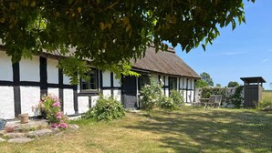 A traditional half-timbered house with a thatched roof, surrounded by a well-maintained garden and a small wooden structure. - 6 Person Holiday Home in Degeberga (Degeberga)