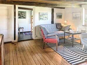 A room with a wooden floor, a grey sofa, a red and black chair, a small table with a glass, and a black and white striped rug. - 6 Person Holiday Home in Degeberga (Degeberga)