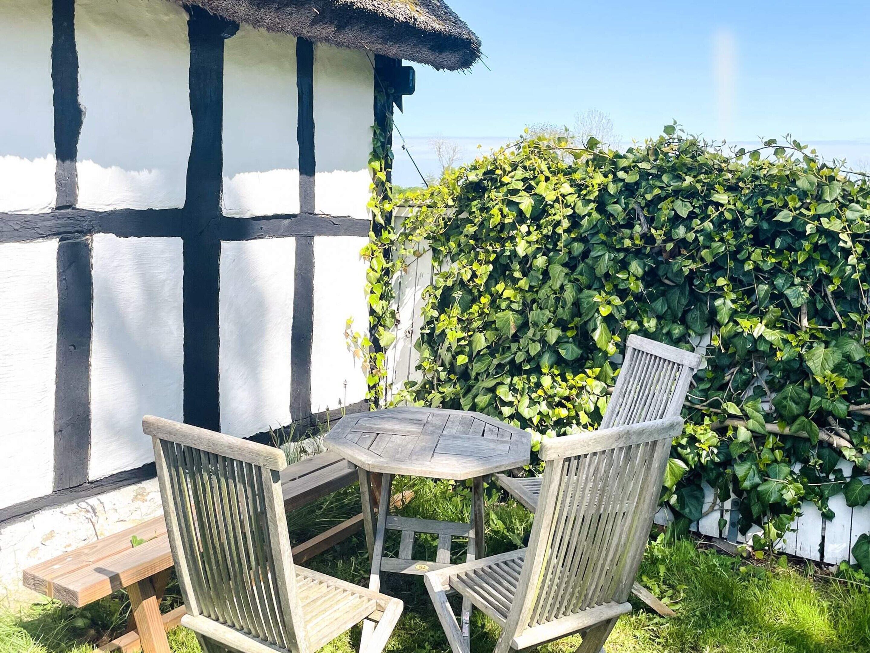 Une table et des chaises en bois se trouvent à l’extérieur d’un bâtiment à la façade blanche et noire.