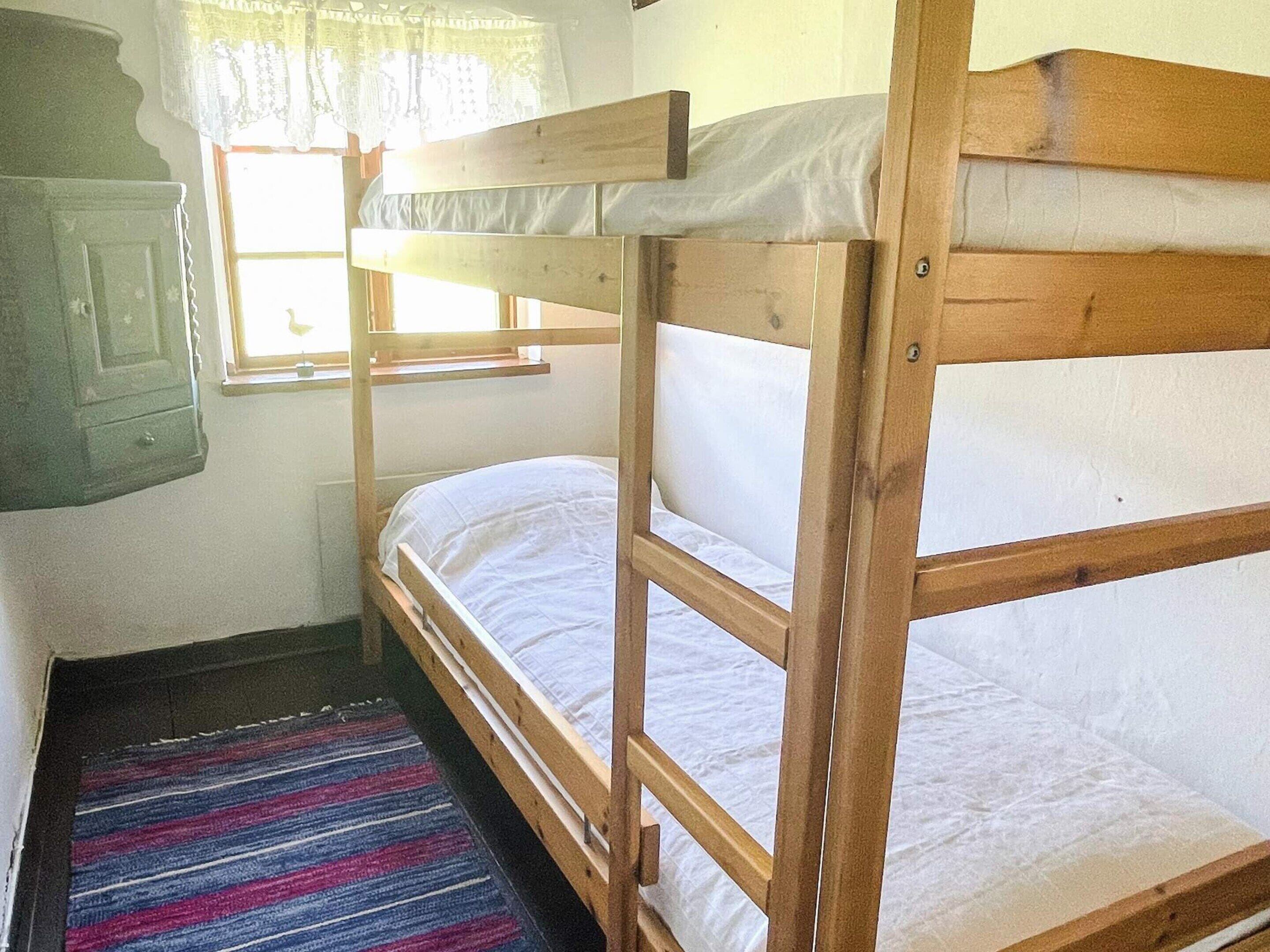 A bunk bed room with a window, a door, and a striped rug.