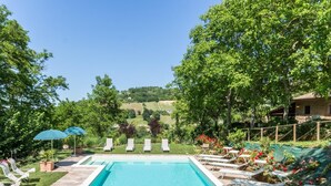 A rectangular swimming pool with a tiled deck, surrounded by lounge chairs and umbrellas. - Belvilla by OYO Villa Dipinti (Serra San Quirico)