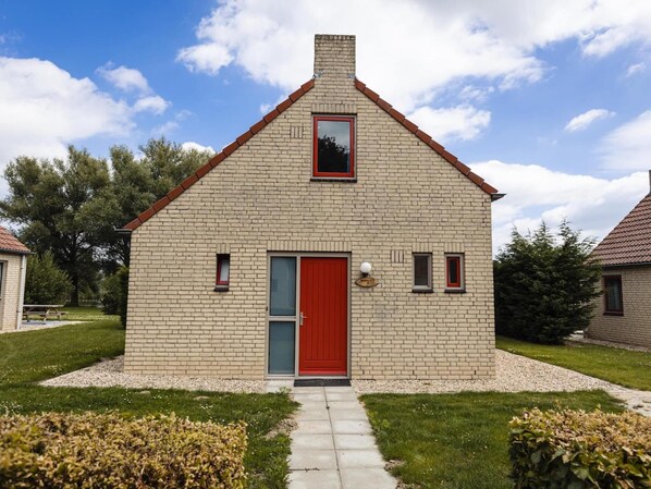 A small brick house with a red door, a small window, and a chimney.
