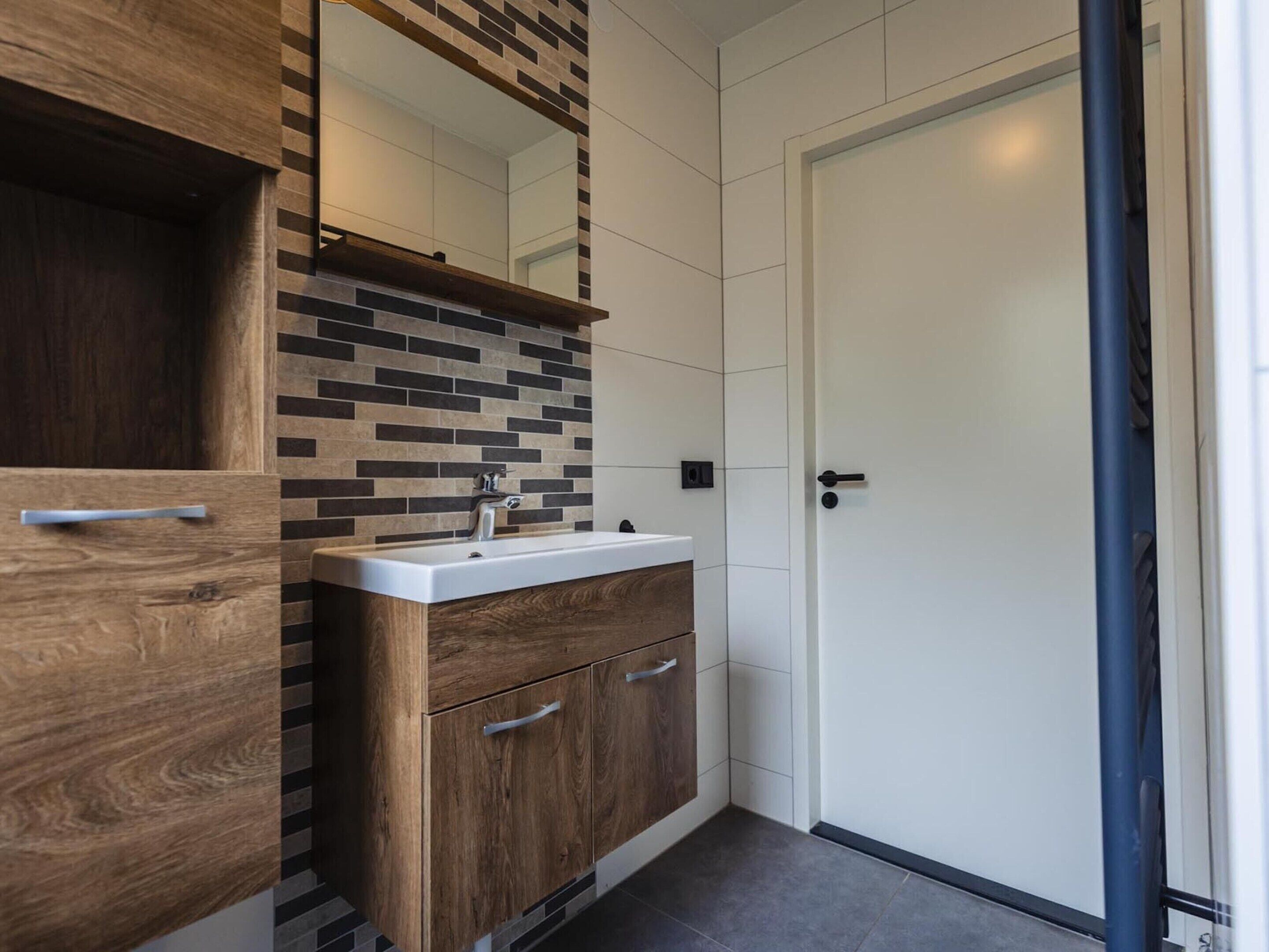 A modern bathroom with a wooden vanity, a white sink, and a tiled backsplash.