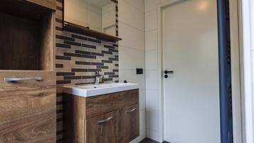 A modern bathroom with a wooden vanity, a white sink, and a tiled backsplash.