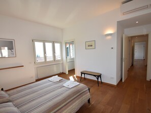 A bedroom with a large bed, a bench, and a view of a hallway. - Apartment in a Prime Location on Lake Maggiore (Verbania)