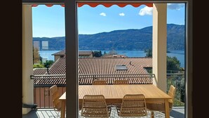 A balcony with a wooden table and chairs, overlooking a lake and mountains. - Apartment in a Prime Location on Lake Maggiore (Verbania)