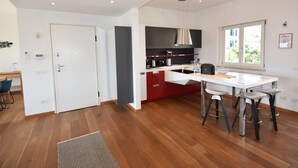 A modern kitchen with a central island, a dining area with bar stools, and a large window providing natural light. - Apartment in a Prime Location on Lake Maggiore (Verbania)