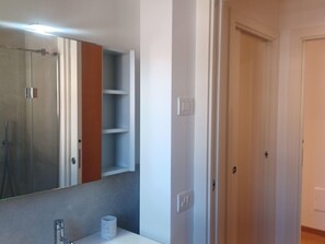 A bathroom with a mirror, a sink, a towel dispenser, and a shower. - Apartment in a Prime Location on Lake Maggiore (Verbania)