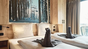 Une chambre d’hôtel avec deux lits, chacun agrémenté d’une sculpture faite de serviettes, d’une tête de lit en bois et d’un tableau représentant une forêt.