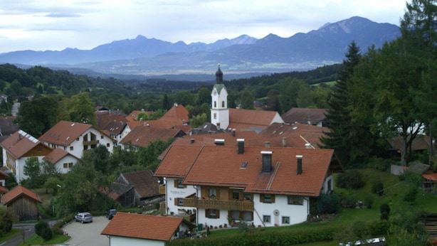 Un village aux maisons traditionnelles, une église dotée d’un clocher, et des montagnes en arrière-plan.