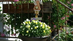 Un arrangement floral en pot, agrémenté d’une pancarte de bienvenue et d’une figurine décorative, le tout posé sur une structure métallique.