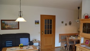 Un salon chaleureux avec un plancher en bois, un canapé, une table à manger avec une chaise, un meuble en bois et une porte avec des panneaux de verre.