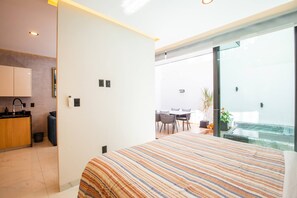 A modern bedroom with a large bed, a kitchen area, and a view of an outdoor patio.