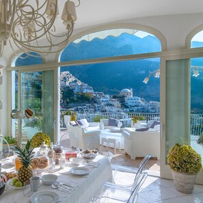 A dining area with a table set for two, overlooking a coastal town with white buildings and a clear blue sky. - Luxurious Villa Elio, Amalfi Coast (Positano)