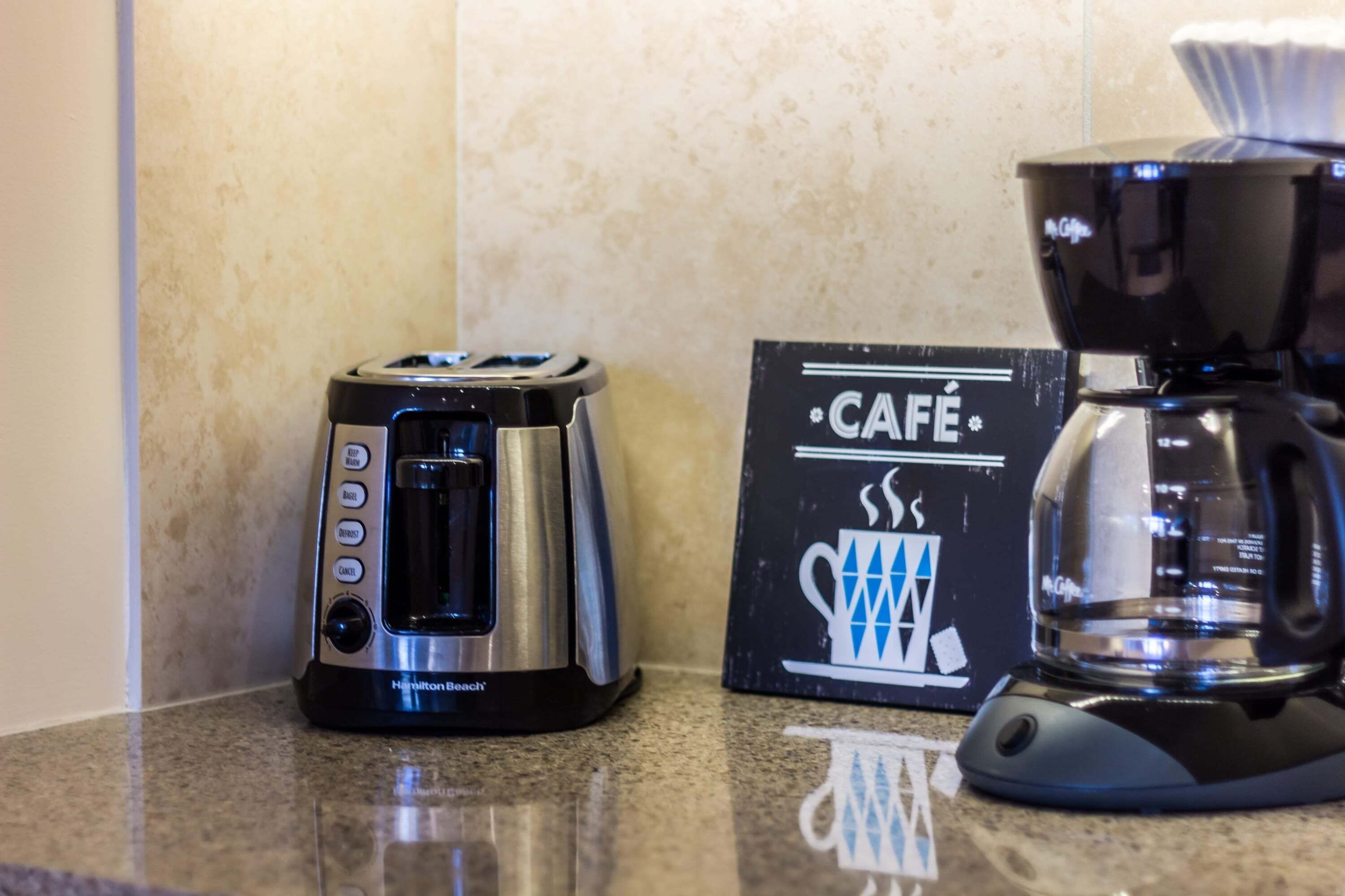 Een Hamilton Beach toaster en een Keurig koffiezetapparaat op een aanrecht, met een 'CAFE' bord.