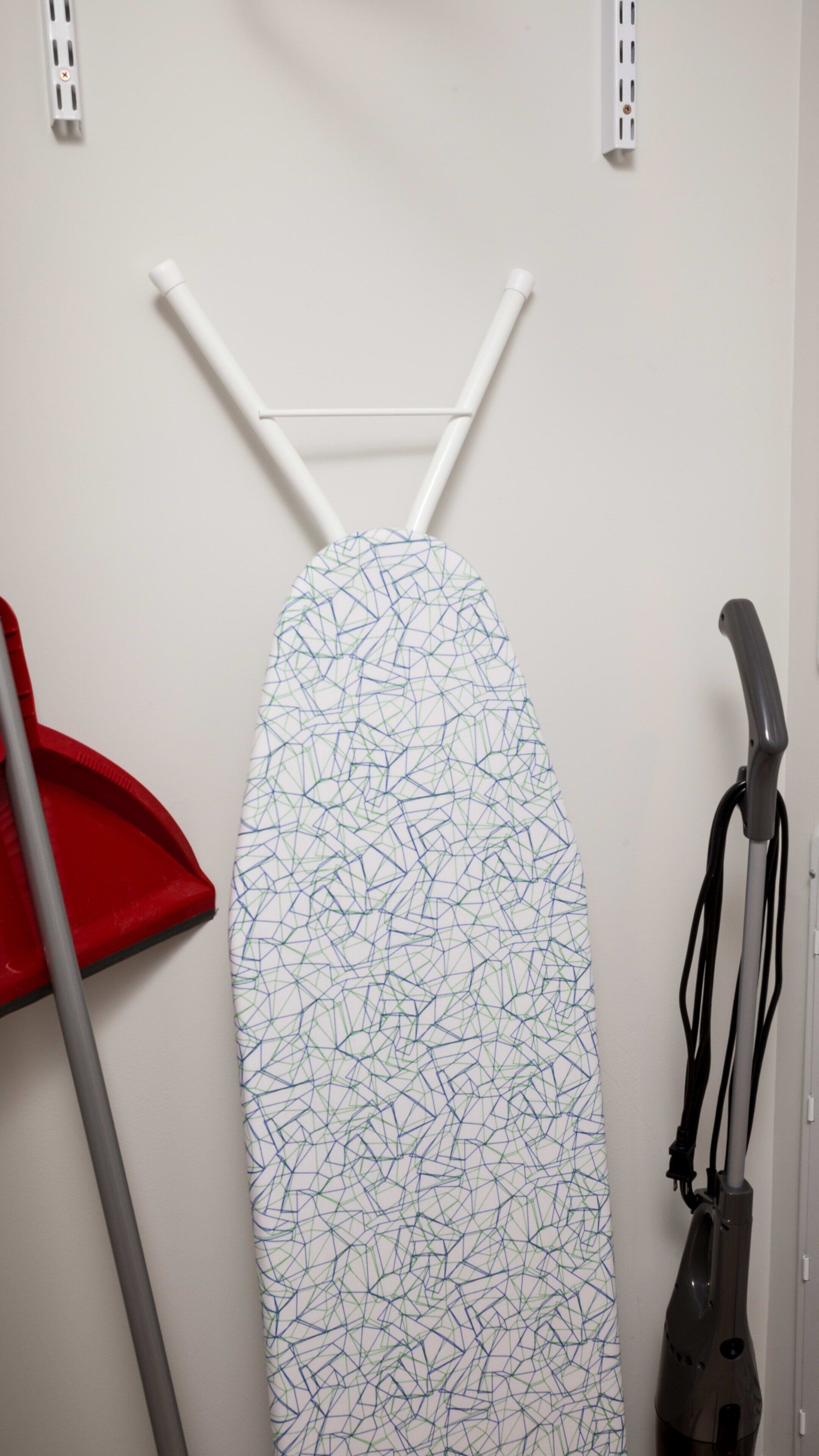 Ein an der Wand befestigtes Bügelbrett, ein rotes Reinigungswerkzeug und ein Staubsauger.