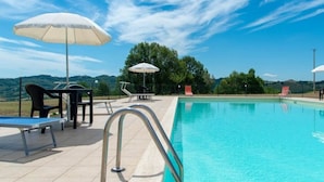 Ein Schwimmbad mit freiem Blick auf die umliegende Landschaft, Sitzgelegenheiten im Freien und Sonnenschirmen.