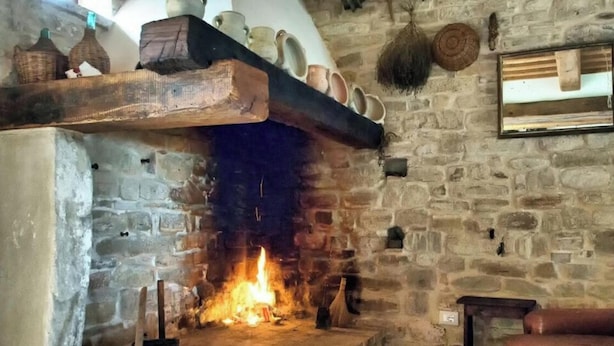 Ein Steinkamin mit Feuer, ein hölzerner Sims mit Keramik und eine Steinsäule mit Besen und Spiegel.