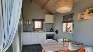 A compact kitchen with white cabinets, a wooden table, and two orange chairs.