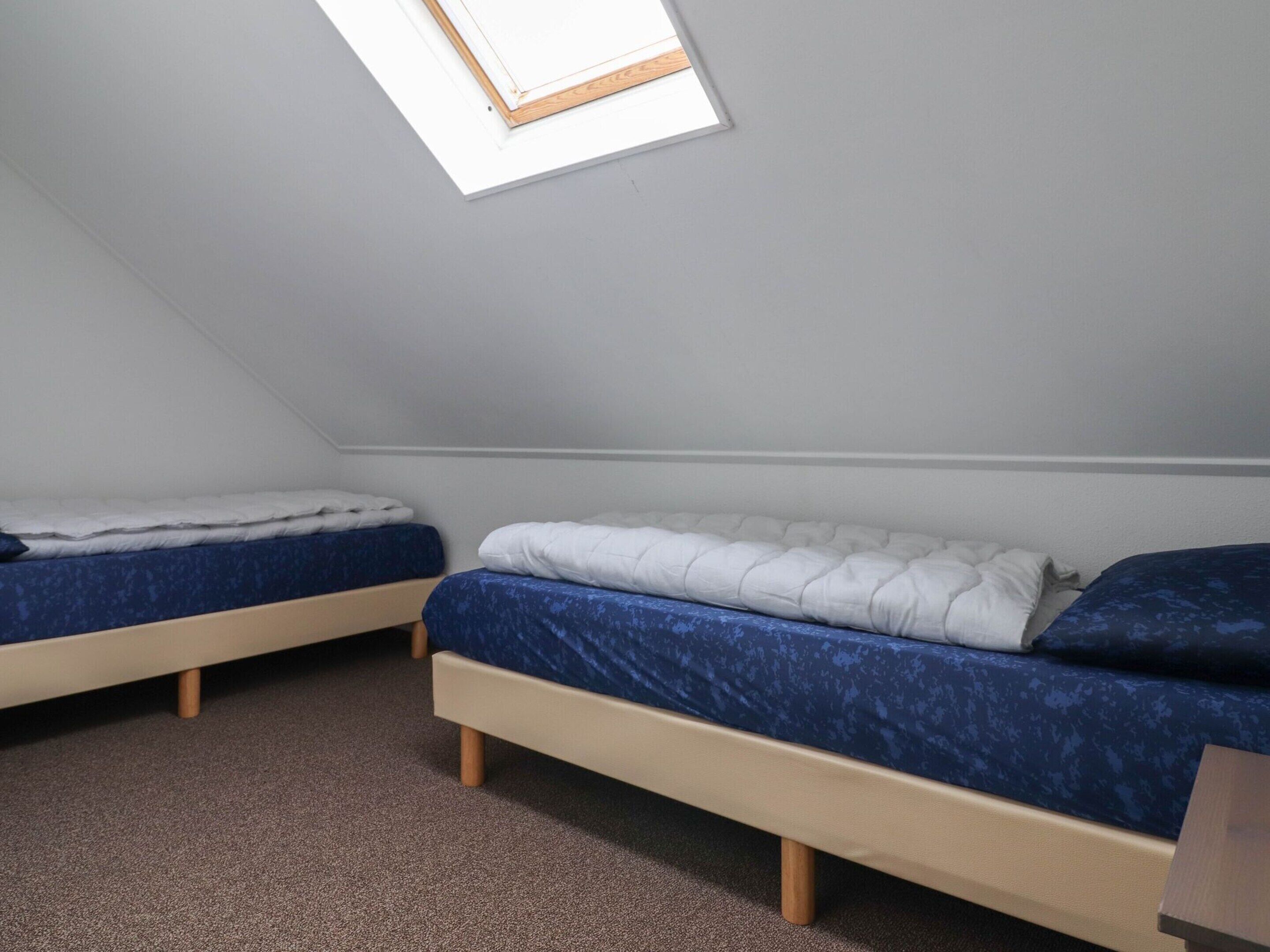 A small, dimly lit room with two bunk beds, a slanted ceiling, and a skylight.
