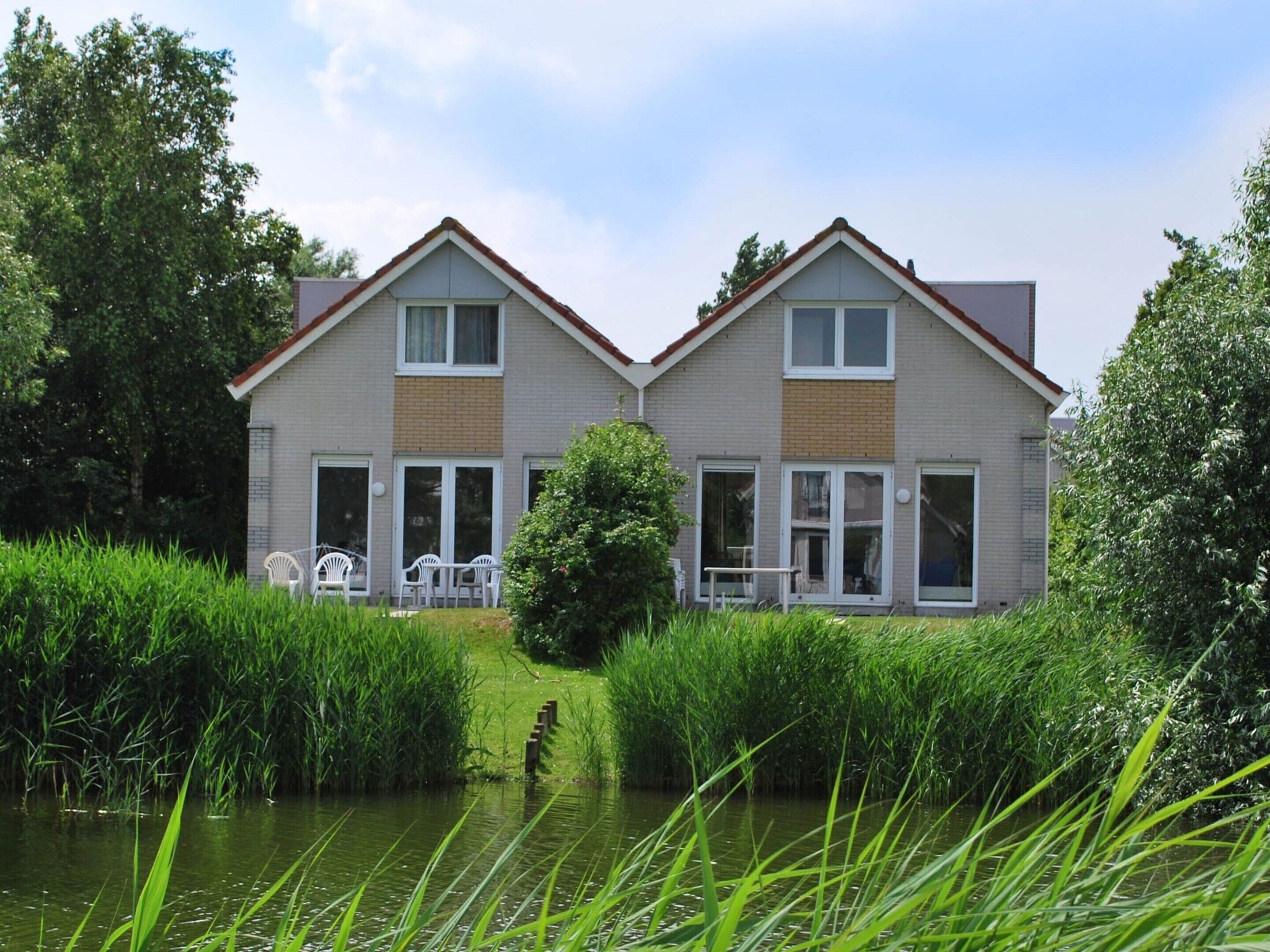 A two-story house with a flat roof, large windows, and a small porch with outdoor furniture.