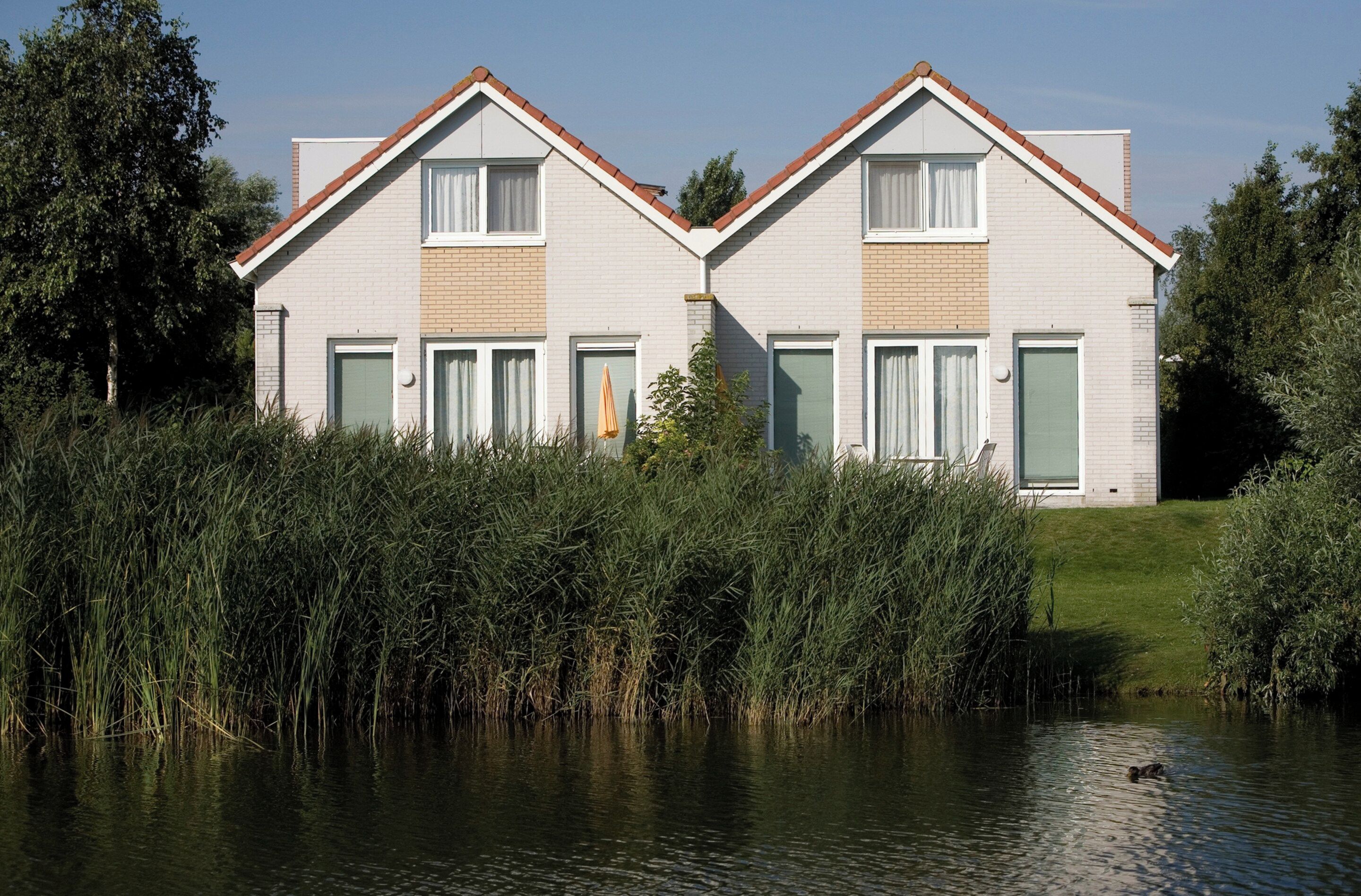 A modern two-story house with a sloped roof, large windows, and a grassy lawn.