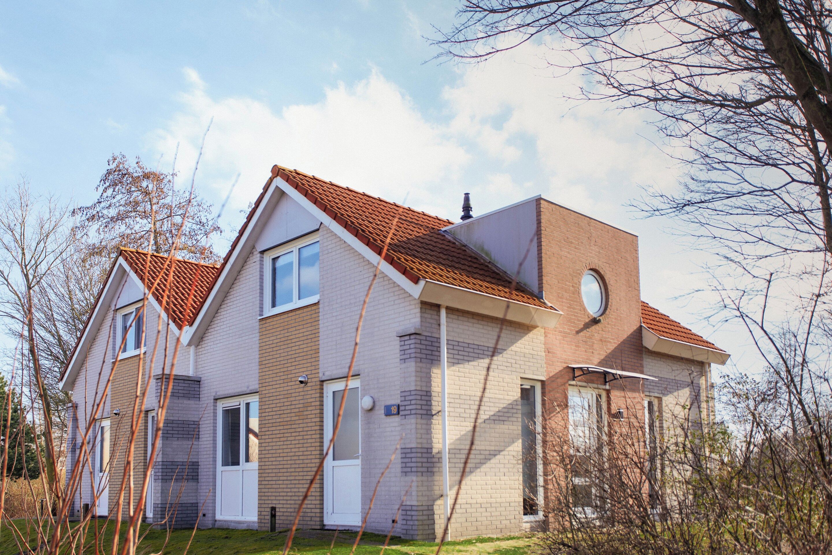 Une maison à deux étages, avec un toit recouvert de tuiles rouges, une façade en briques et une fenêtre circulaire à l’étage supérieur.