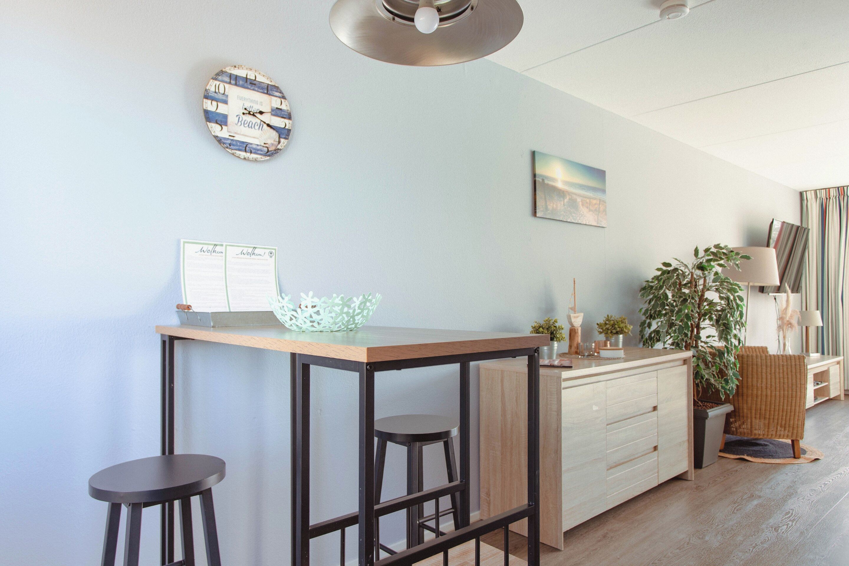 Una cocina moderna con una isla de madera, taburetes de bar, una lámpara colgante y un reloj decorativo.