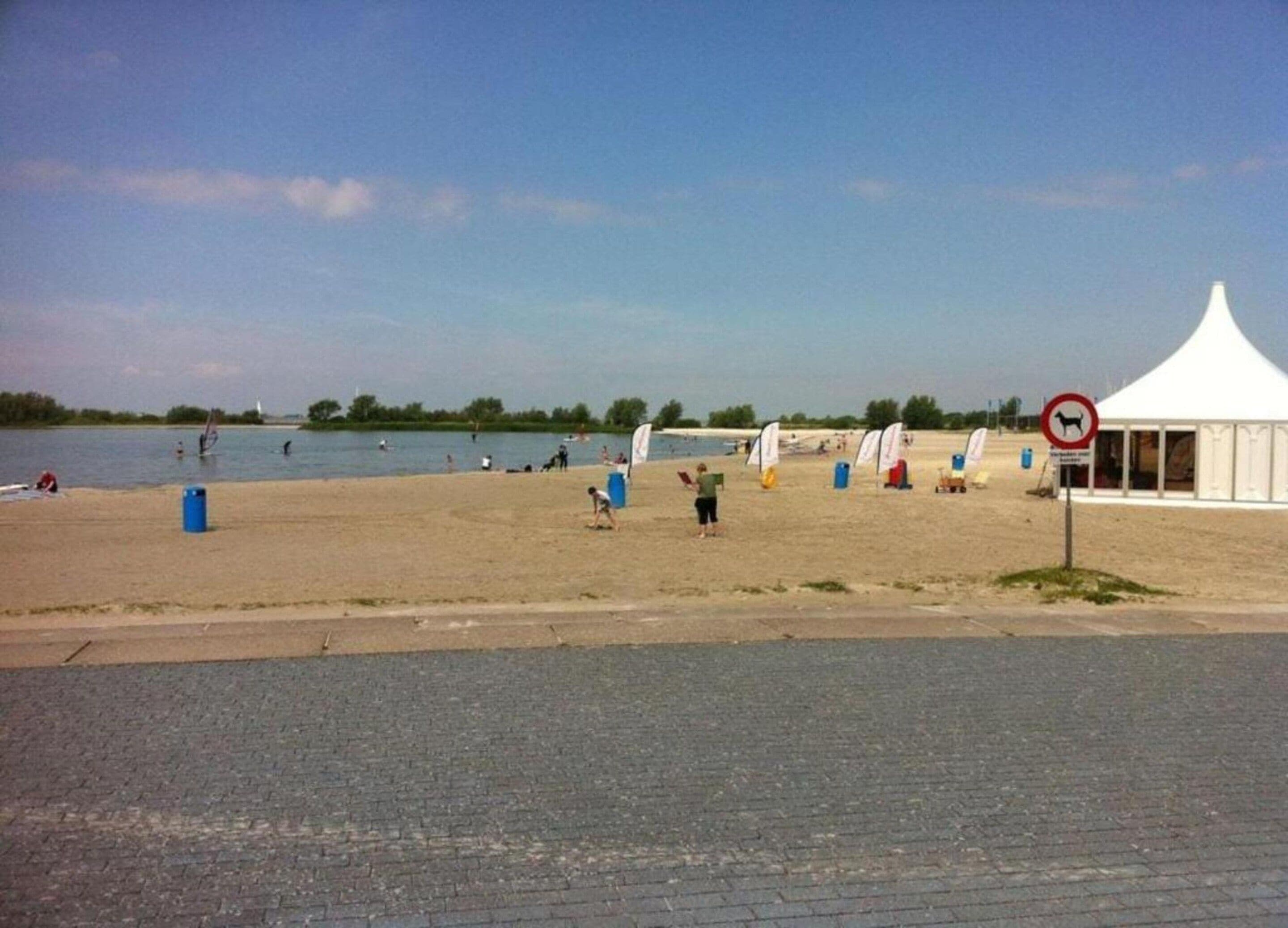 A beach with a tent, a no dogs sign, and people engaging in water activities.