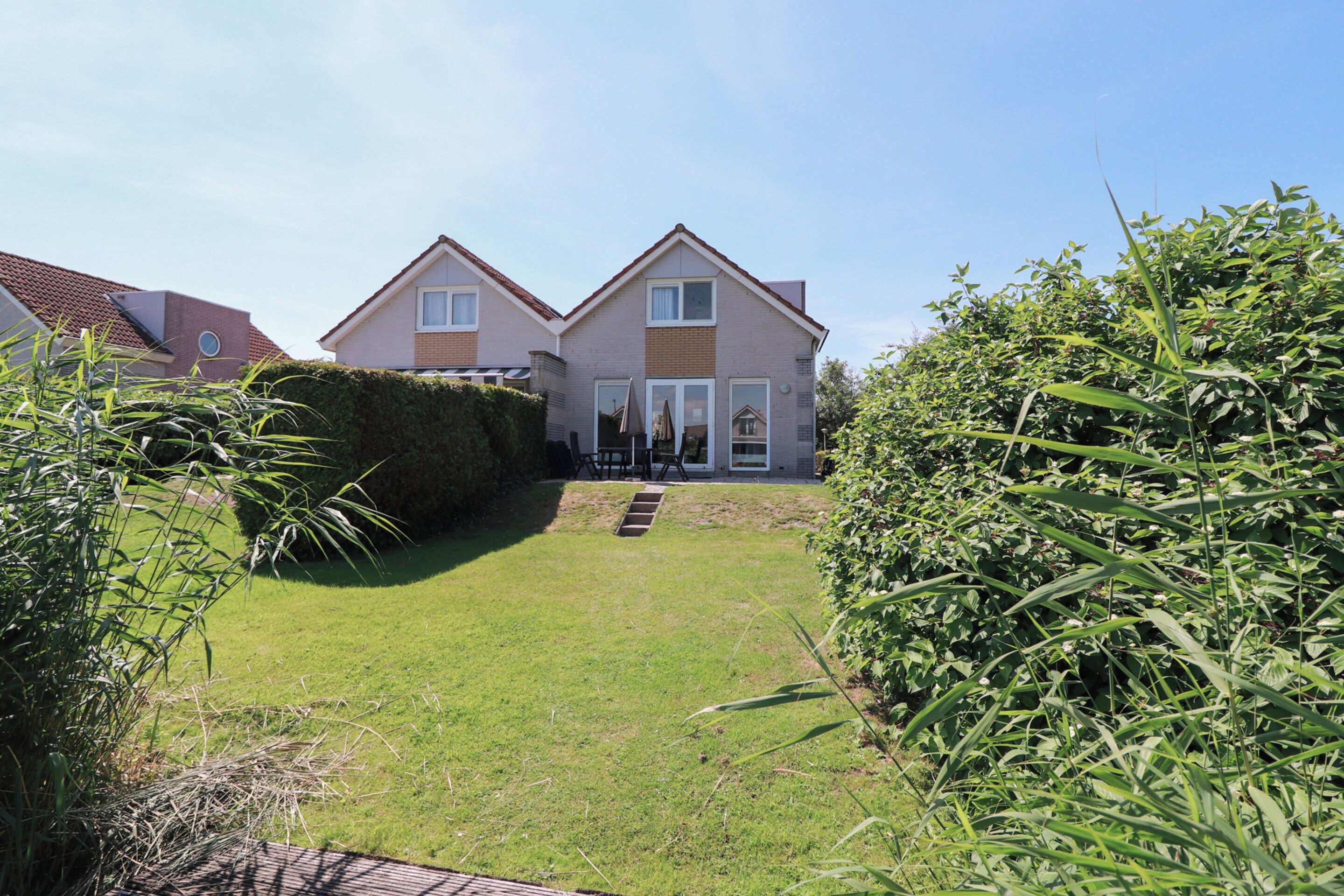 A two-story residential building with a front garden, a visible staircase leading to the entrance, and a clear sky.