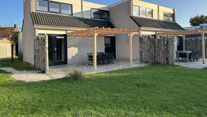 A modern two-story house with a covered patio area, a fenced backyard, and a well-maintained lawn. - Holiday Home on Texel With Garden Terrace (De Cocksdorp)