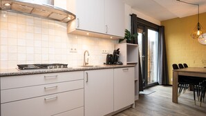 A modern kitchen with white cabinets, a stainless steel range hood, and a built-in stove. - Holiday Home on Texel With Garden Terrace (De Cocksdorp)