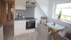 A compact kitchen with a built-in oven, a coffee maker, and a small dining area with a table and chairs. - Gerda in the Michaela House (Borkum)