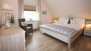 A bedroom with a bed, a chair, a nightstand, a lamp, and a window with curtains. - Gerda in the Michaela House (Borkum)
