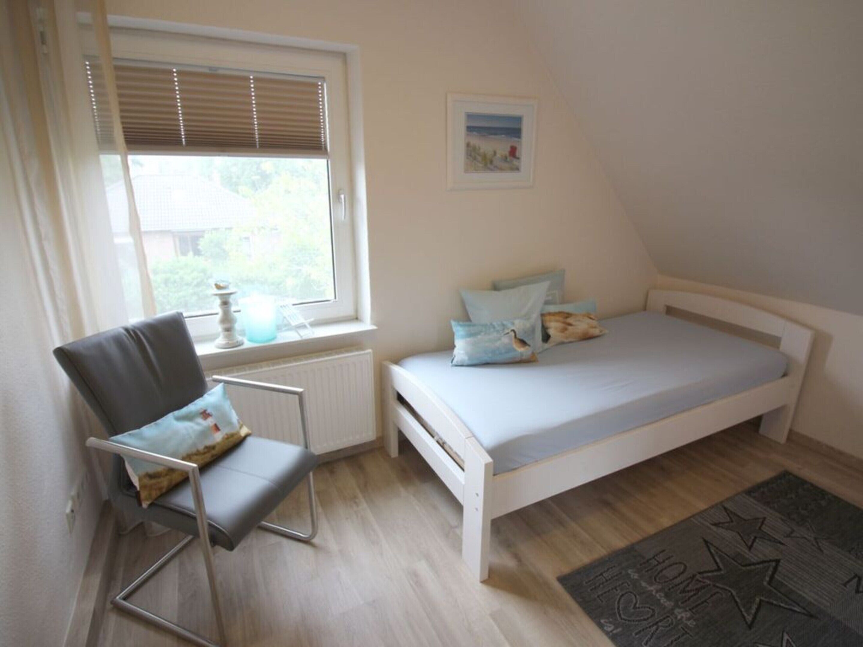 A bedroom with a single bed, a chair, a radiator, a window with blinds, and a picture on the wall.