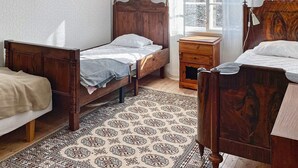 A room with two wooden beds, a small bedside table, a patterned rug, and a window with a view of trees. - 5 Person Holiday Home in Gamleby (Gamleby)