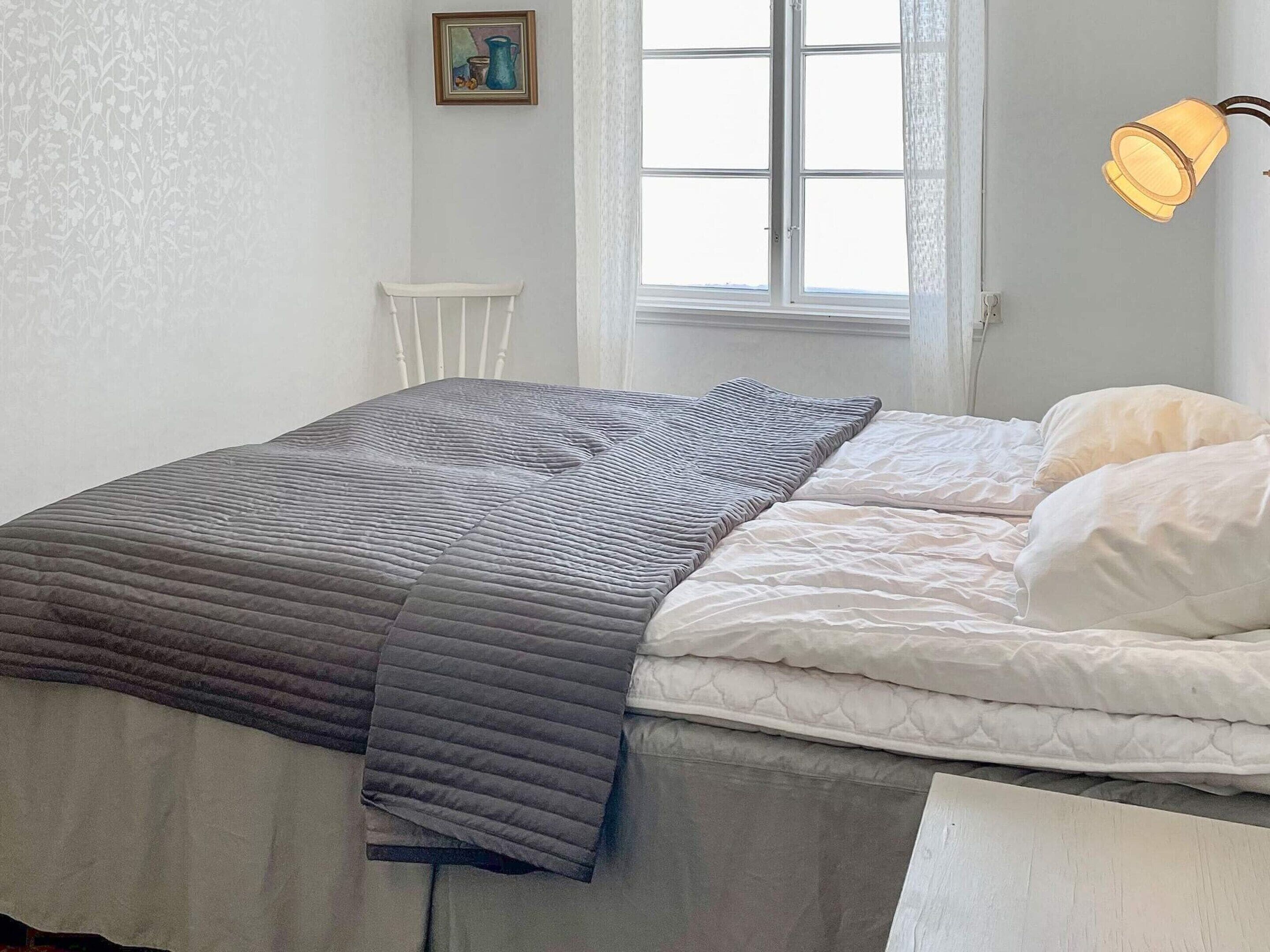 A bedroom with a bed, a window, a chair, and a wall-mounted lamp.