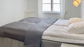 A bedroom with a bed, a window, a chair, and a wall-mounted lamp.