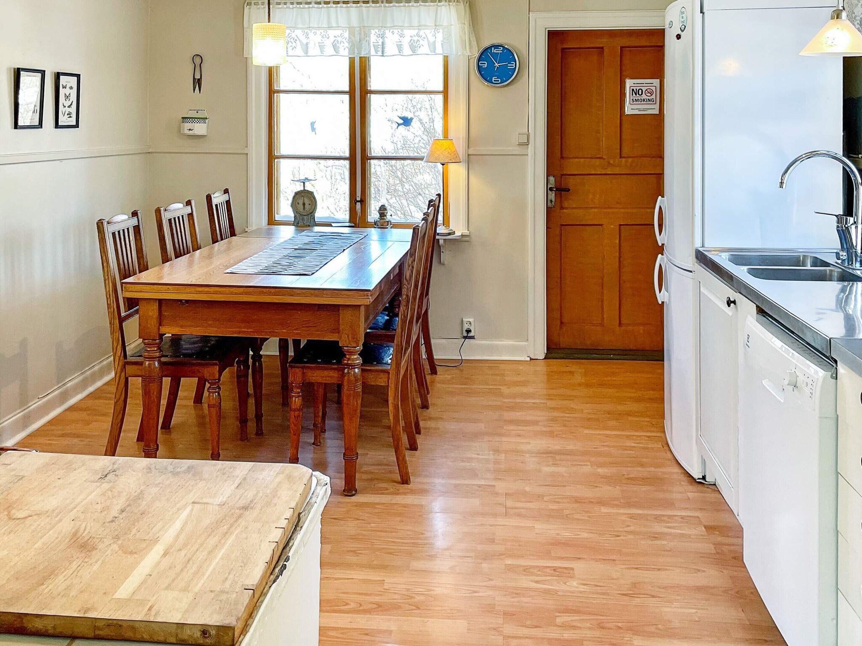 A dining area with a wooden table and chairs, a clock, and a kitchen with a sink and dishwasher.