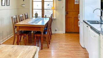 A dining area with a wooden table and chairs, a clock, and a kitchen with a sink and dishwasher.