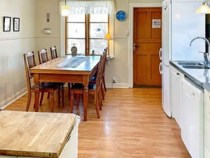 A dining area with a wooden table and chairs, a clock, and a kitchen with a sink and dishwasher. - 5 Person Holiday Home in Gamleby (Gamleby)