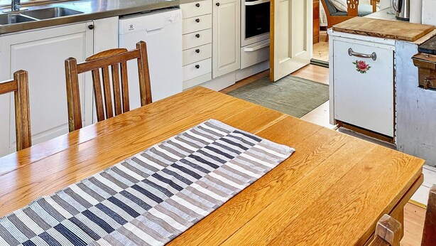 A kitchen with white cabinets, a wooden dining table, and a patterned rug. - 5 Person Holiday Home in Gamleby (Gamleby)