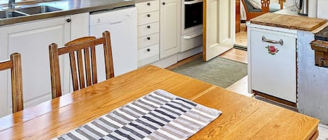 Una cocina con armarios blancos, una mesa de comedor de madera y un tapete estampado.