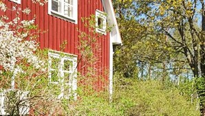 A red barn with white trim and windows, surrounded by greenery and trees. - 5 Person Holiday Home in Gamleby (Gamleby)