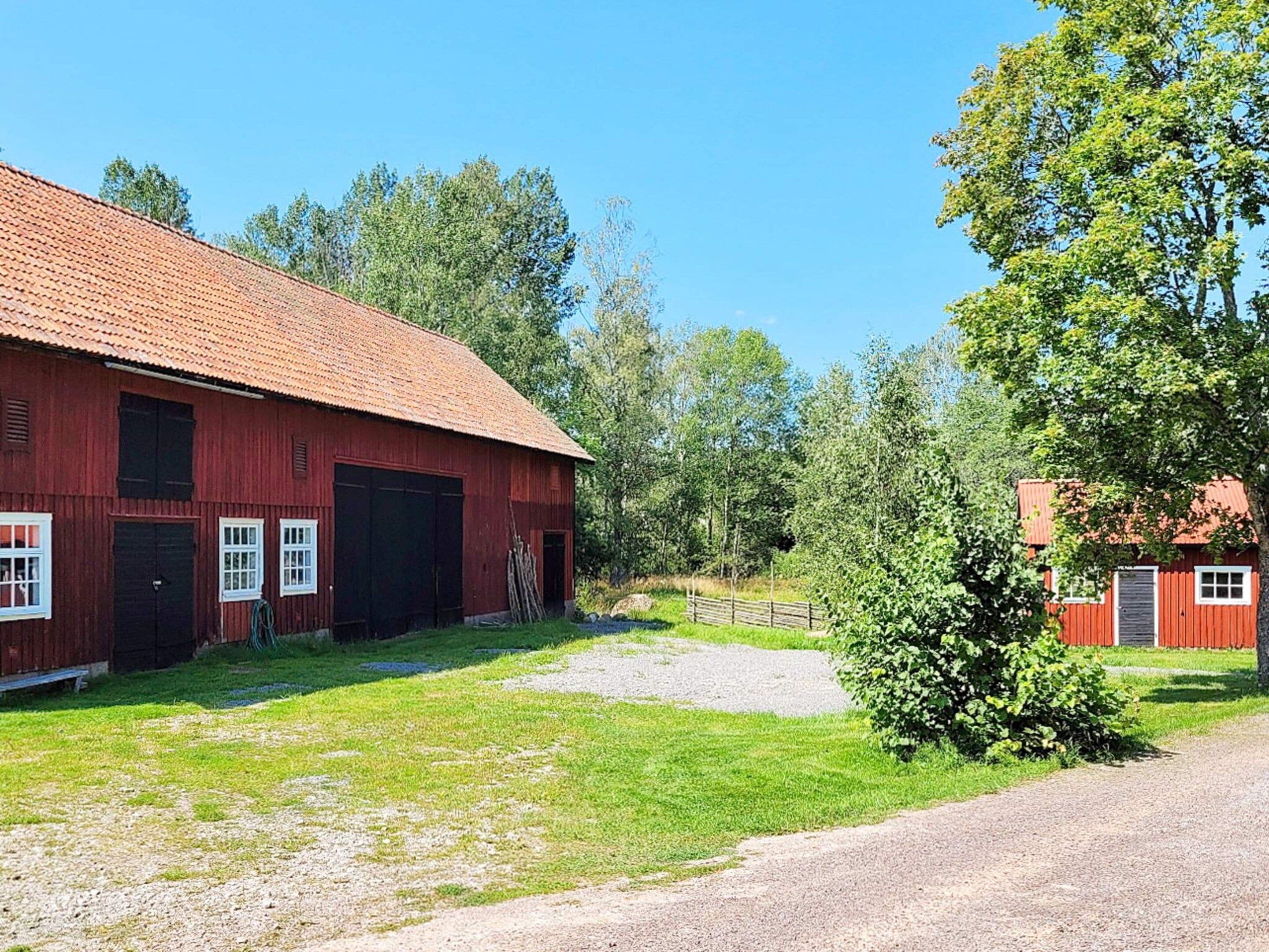 A red barn with a gravel driveway and a small green bush in the foreground.