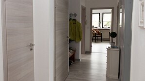 A hallway with a wooden floor, a coat rack with a green jacket, a chair, and a small potted plant. - Long Comfortable Holiday Residence (Süderlügum)