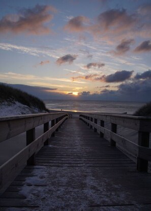 A wooden boardwalk leading to the sea with a sunset in the background. - Long Comfortable Holiday Residence (Süderlügum)
